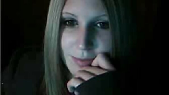 Blondīne ar zilām acīm smaida, kad viņas mutē ir ielikts liels gailis